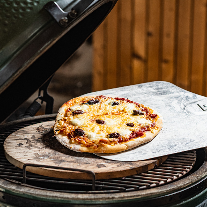 Pizza on a ceramic baking stone in the Big Green Egg kamado